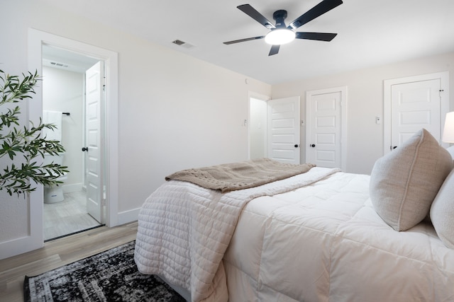 bedroom featuring connected bathroom, ceiling fan, visible vents, baseboards, and light wood-type flooring