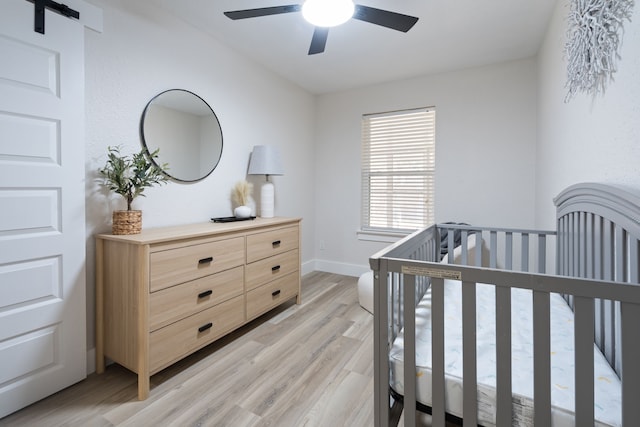 6410 Symphony Ln, Dallas, TX 75227 - bedroom featuring light wood-style flooring, a crib, a barn door, ceiling fan, and baseboards