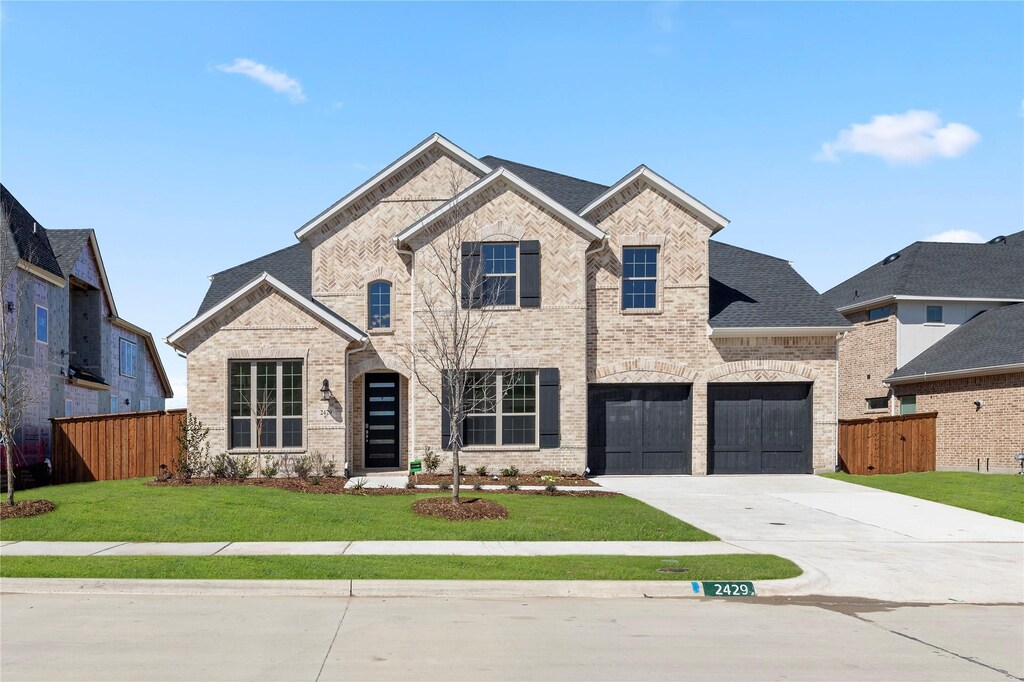 french country home with driveway, brick siding, fence, and a front lawn