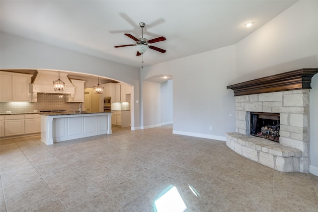816 Sandbox Dr, Little Elm, TX 76227 - unfurnished living room featuring arched walkways, ceiling fan, a sink, a fireplace, and light tile patterned floors