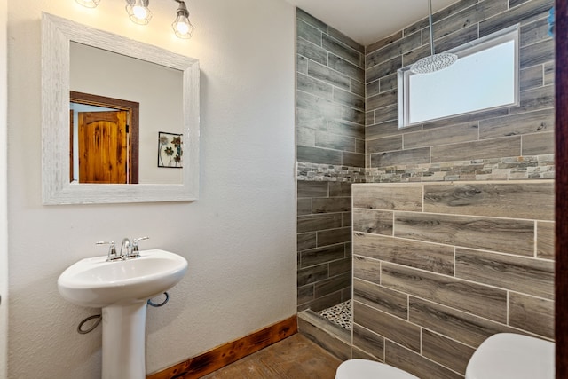 full bathroom featuring toilet, baseboards, a tile shower, and a sink