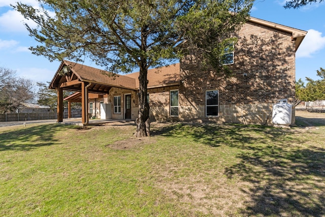 rear view of property featuring brick siding, a lawn, a patio, and fence