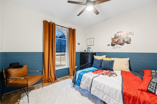 carpeted bedroom with wooden walls, a wainscoted wall, and ceiling fan
