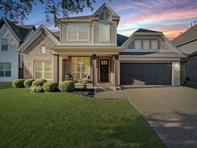 view of front of house featuring an attached garage, covered porch, concrete driveway, a lawn, and brick siding