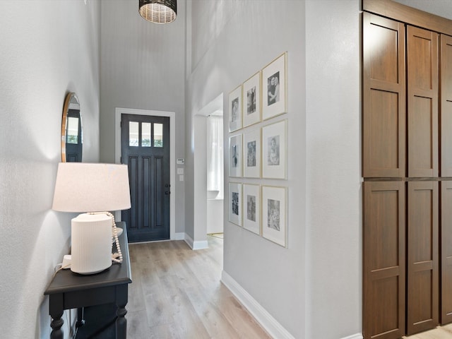 entryway with baseboards, a high ceiling, and light wood-style flooring