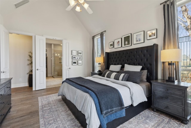 bedroom featuring high vaulted ceiling, ensuite bathroom, visible vents, wood finished floors, and baseboards