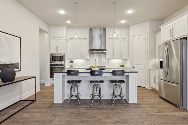 kitchen with wall chimney range hood, white cabinets, a breakfast bar area, stainless steel appliances, and backsplash