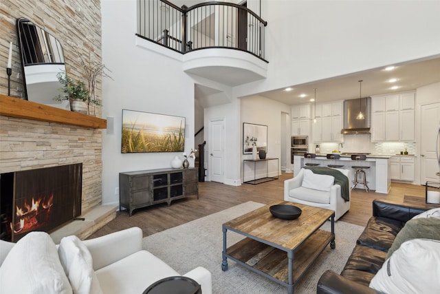 living area with light wood-type flooring, baseboards, recessed lighting, a fireplace, and a high ceiling