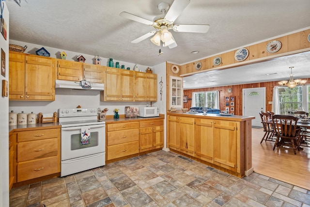 kitchen with white appliances, wooden walls, a peninsula, stone finish floor, and under cabinet range hood
