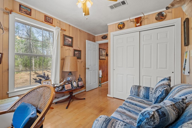 interior space featuring visible vents, ceiling fan, wood walls, crown molding, and light wood-type flooring
