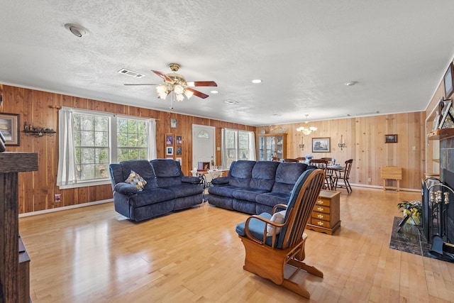 living room with light wood finished floors, ceiling fan with notable chandelier, and a textured ceiling