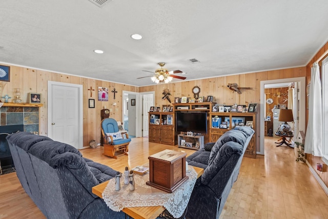 living room featuring a fireplace, light wood-style flooring, a ceiling fan, and visible vents