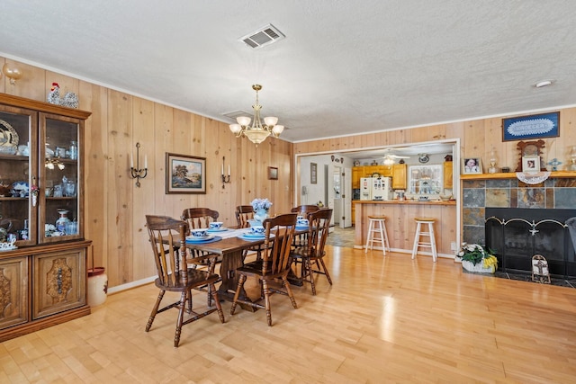 dining space with light wood finished floors, visible vents, a tiled fireplace, an inviting chandelier, and a textured ceiling