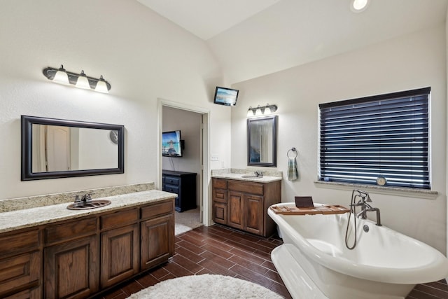 full bathroom with two vanities, a sink, vaulted ceiling, and a freestanding tub
