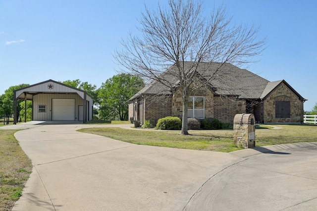 view of front facade with a front yard, stone siding, a garage, an outbuilding, and driveway