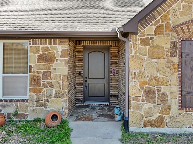 view of exterior entry with brick siding, stone siding, and roof with shingles