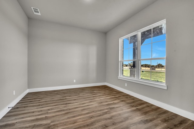 empty room featuring wood finished floors, visible vents, and baseboards