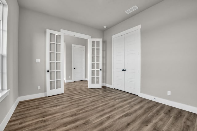 unfurnished bedroom with visible vents, baseboards, french doors, wood finished floors, and a closet