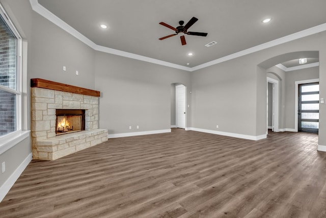 unfurnished living room with a ceiling fan, visible vents, baseboards, arched walkways, and a stone fireplace