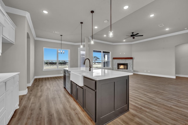 kitchen featuring white cabinetry, a fireplace, a sink, dishwasher, and ceiling fan with notable chandelier