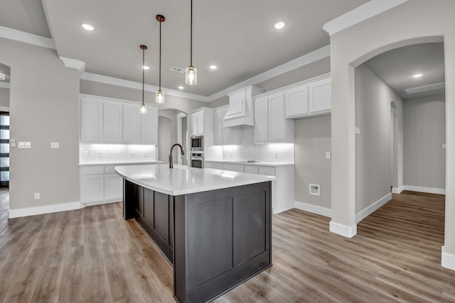kitchen featuring a kitchen island with sink, light wood-style floors, arched walkways, and a sink
