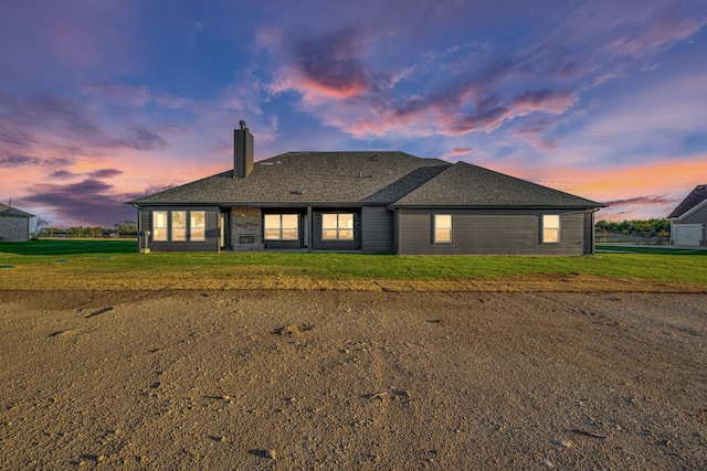 back of property at dusk featuring a lawn, roof with shingles, and a chimney