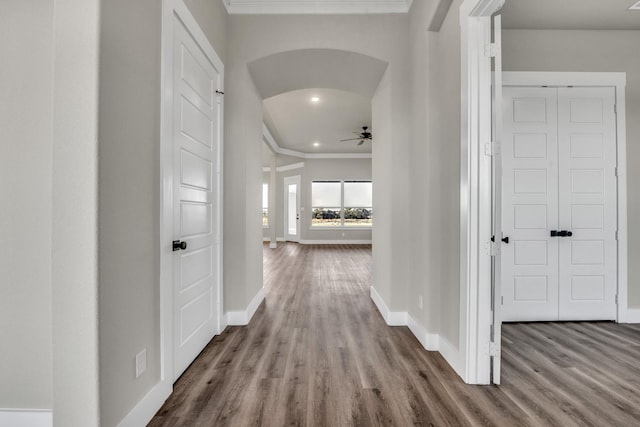 hallway with crown molding, wood finished floors, arched walkways, and baseboards