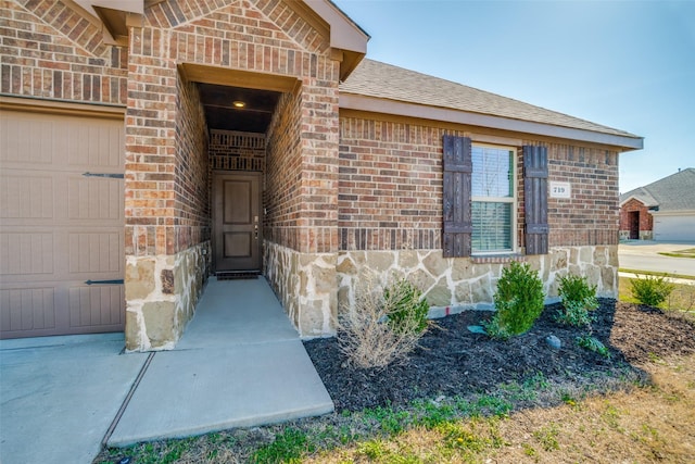 view of exterior entry featuring brick siding, stone siding, a garage, and roof with shingles