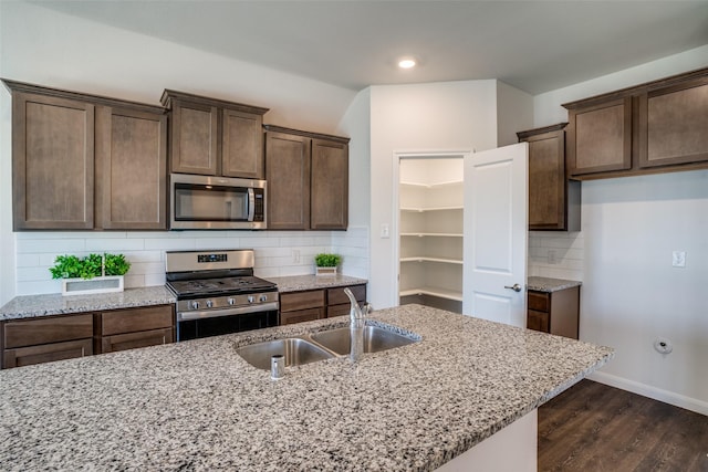 kitchen featuring backsplash, dark wood-type flooring, light stone countertops, appliances with stainless steel finishes, and a sink
