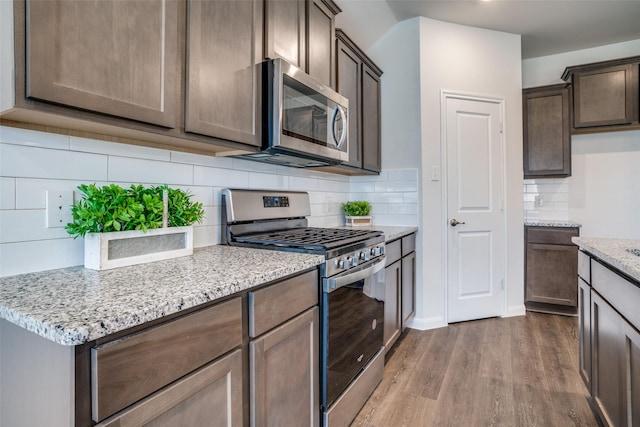 kitchen with dark brown cabinets, light stone counters, decorative backsplash, appliances with stainless steel finishes, and wood finished floors