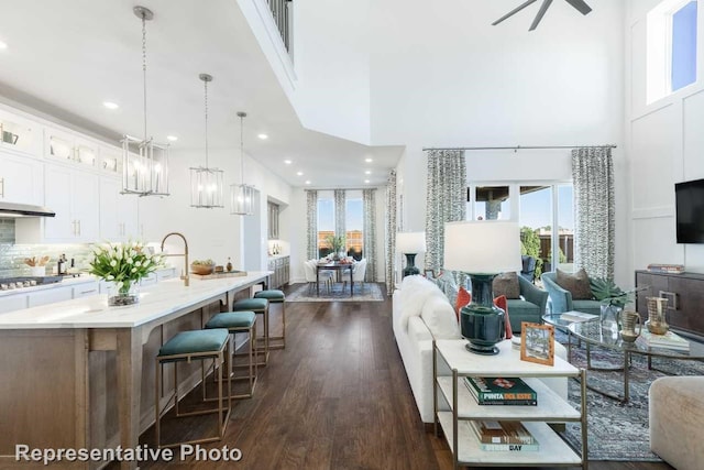 living room with dark wood-style floors, a high ceiling, recessed lighting, and ceiling fan with notable chandelier