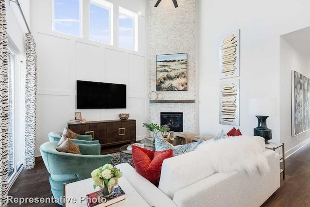 living area with baseboards, a large fireplace, a high ceiling, and dark wood-style flooring
