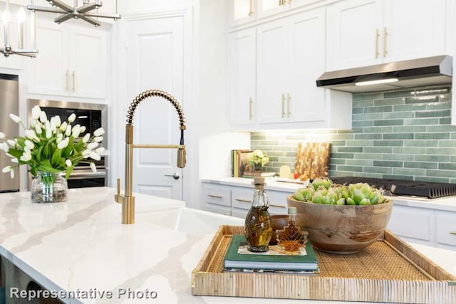 details featuring white cabinets, light stone counters, under cabinet range hood, and decorative backsplash
