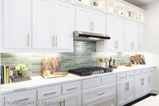 kitchen with glass insert cabinets, stainless steel gas stovetop, under cabinet range hood, light countertops, and white cabinetry