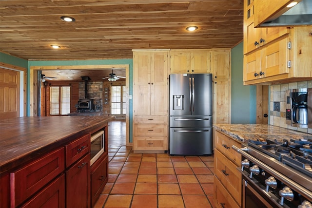 kitchen featuring a wood stove, wood ceiling, stainless steel appliances, butcher block countertops, and backsplash