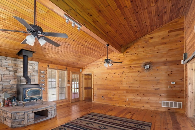 unfurnished living room featuring visible vents, lofted ceiling with beams, a wood stove, a ceiling fan, and hardwood / wood-style floors