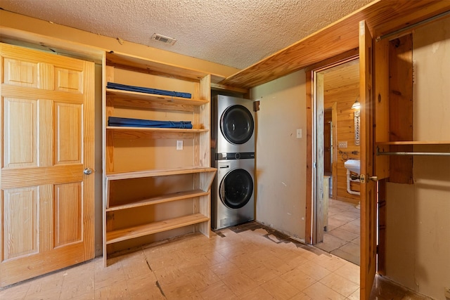 laundry area featuring laundry area, a textured ceiling, visible vents, stacked washing maching and dryer, and tile patterned floors