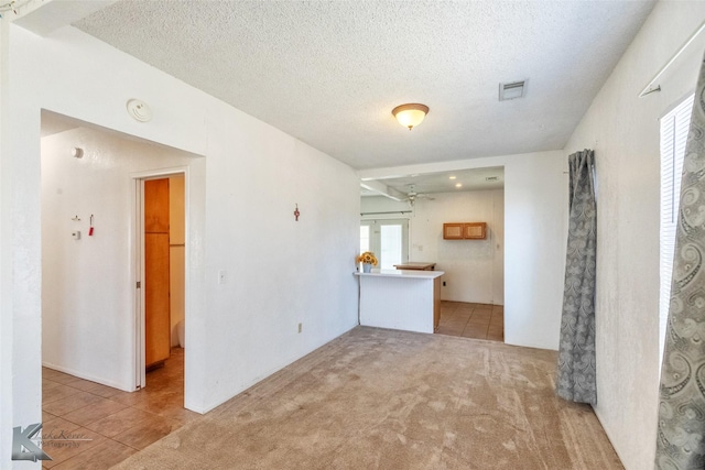 unfurnished living room with light tile patterned floors, light colored carpet, visible vents, and a textured ceiling