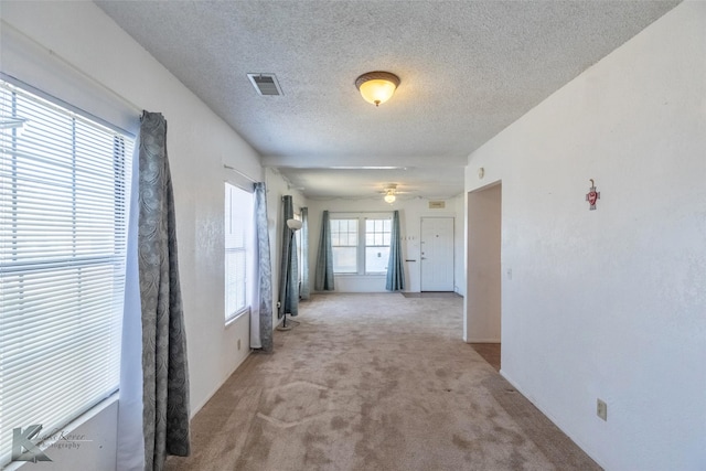 hallway with visible vents, light colored carpet, and a textured ceiling