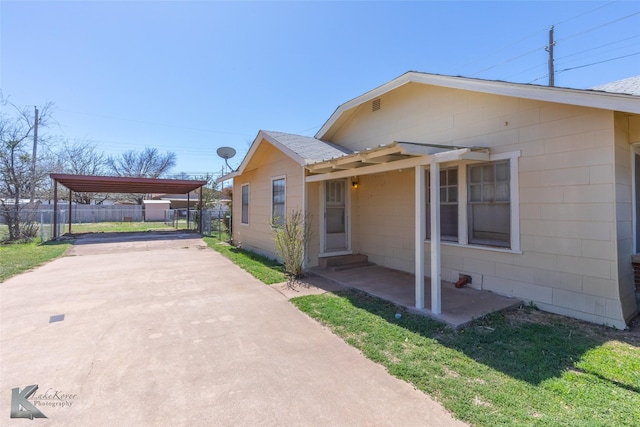 view of property exterior featuring a patio, fence, concrete driveway, a carport, and a lawn