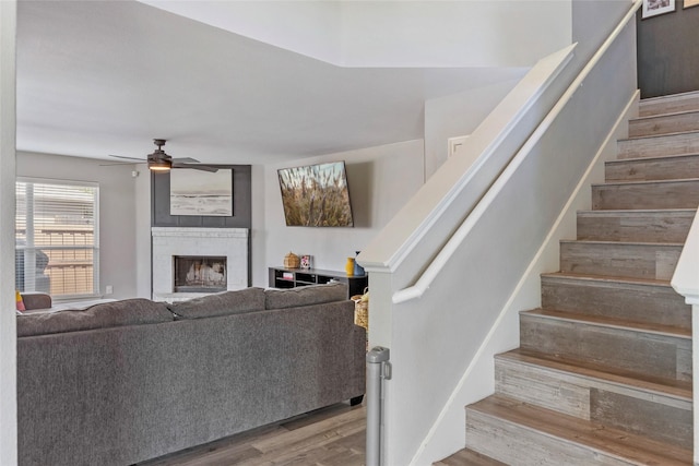 living room featuring a ceiling fan, stairway, wood finished floors, and a large fireplace