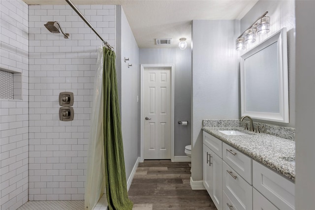 full bath featuring visible vents, toilet, a tile shower, wood finished floors, and vanity