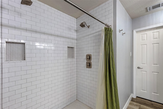 bathroom with wood finished floors, visible vents, a tile shower, and a textured ceiling