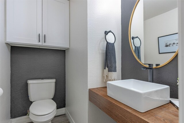 half bath with a sink, baseboards, toilet, and a textured wall