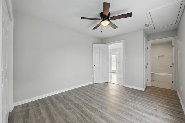 unfurnished bedroom with visible vents, attic access, wood finished floors, and baseboards