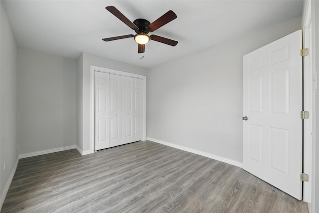 unfurnished bedroom with ceiling fan, baseboards, wood finished floors, and a closet