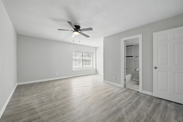 unfurnished bedroom featuring baseboards, ensuite bathroom, wood finished floors, and a ceiling fan