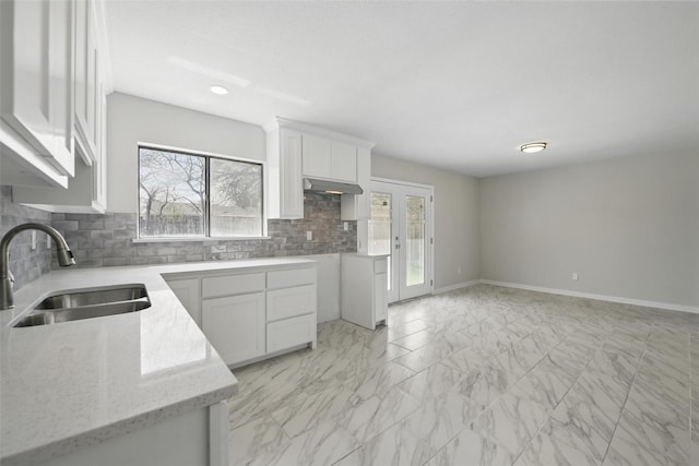kitchen featuring white cabinets, marble finish floor, light stone counters, backsplash, and a sink
