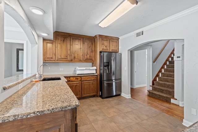 2508 Carnation Ave, Fort Worth, TX 76111 - kitchen featuring stainless steel fridge, a sink, arched walkways, brown cabinetry, and light stone counters