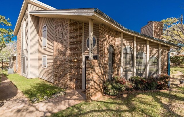view of property exterior with brick siding, central air condition unit, and a chimney